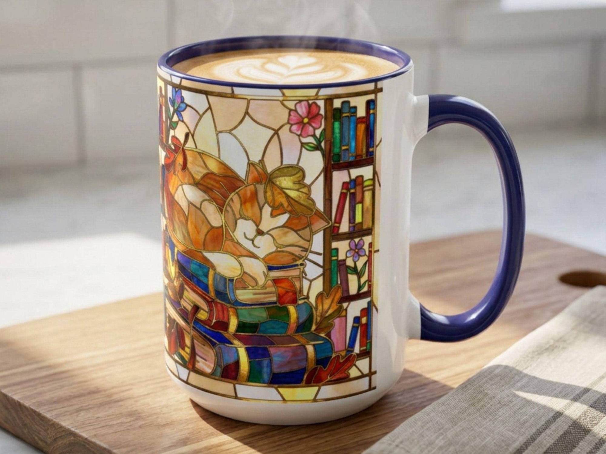 A white ceramic coffee mug with a dark blue handle and rim, featuring a colorful stained-glass style illustration of a cat reading books. The mug is filled with latte art and sits on a wooden cutting board.